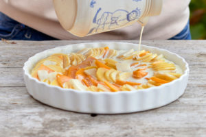 Prepare a gratin of potatoes, pumpkin and Jerusalem artichokes, pour the sliced ingredients in a buttered baking pan with milk and cream from a jug Prepare a gratin of potatoes, pumpkin and Jerusalem artichokes, pour the sliced ingredients in a buttered baking pan with milk and cream from a jug